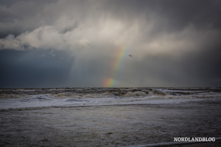 Die Nordsee tobt extrem aufgewühlt und über dem Meer ist ein Regenbogen zu erkennen