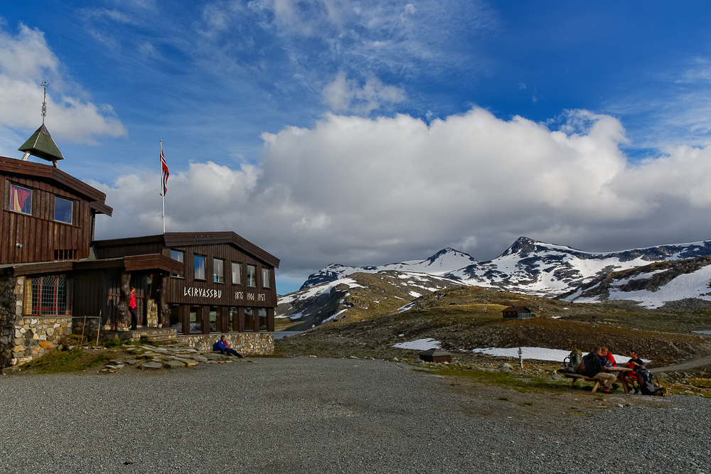 Bild mit schneebedeckten Gipfeln, blauem Himmel und der norwegischen DNT Hütte Leirvassbu im Jotunheimen